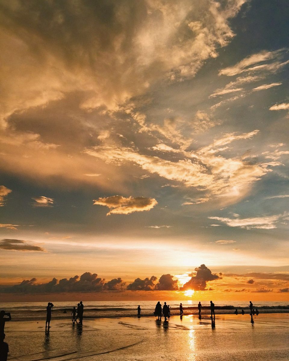 A family silhouetted on a beach against a warm sunset sky.
