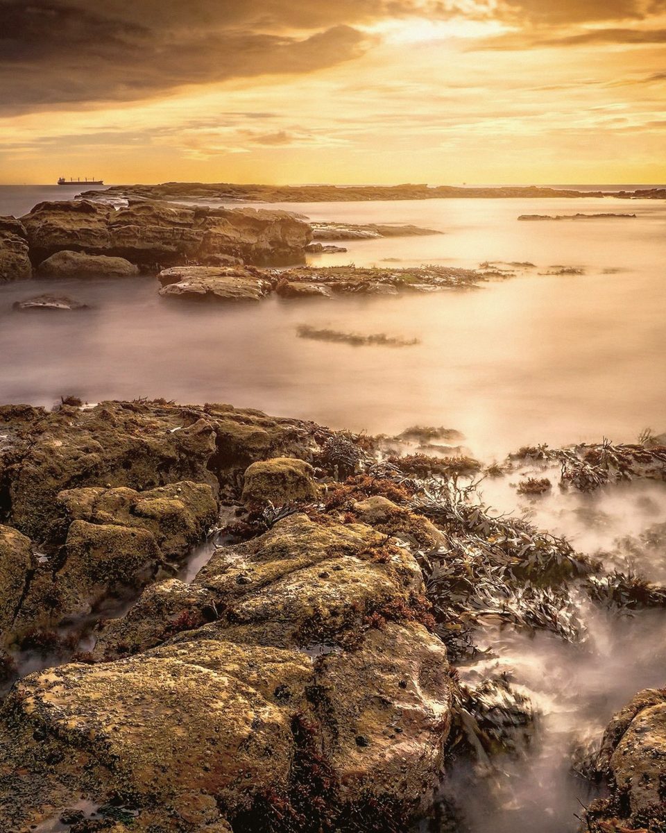 A rocky shoreline at golden hour with calm water at long exposure.